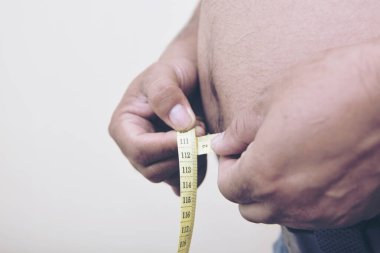 Şişman adam vücudundaki yağ oranına bak. Şişman ya da obez geçmişi için mezurayla ölçüm yapıyor.