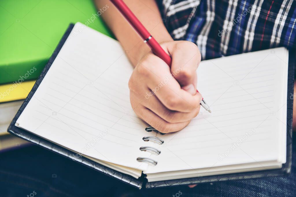 A young boy writing on notebook diary in selective focus.