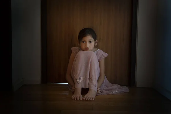 悲しみは少女を怖がらせた 光のドアの前の暗い廊下に座っている子供 恐怖と優柔不断だ 子供の概念に対する家庭内暴力 — ストック写真
