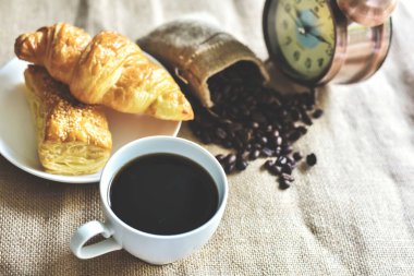 Kahve molası zamanı. Sıcak siyah amerikan kahvesi ve kruvasan pastanesi ve çuval bezinin üstünde ferahlatıcı bir öğleden sonra. Dünya Gıda ve İçecek Konsepti.