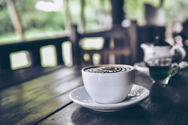Coffee on old wooden table with blur green nature background,latte art lover time concept.