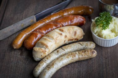 Seçici odaklanma. Izgara sosis ve ahşap tahtada baharat ve otlarla patates püresi. Kesme tahtasında domuz sucuğu. Izgara barbekü konsepti..