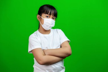 Koronavirüsü korumak için beyaz tişörtlü Asyalı kız çocuğu, Covid-19. Yeşil arka planda kollarını kavuşturuyor.                                                                                                                               