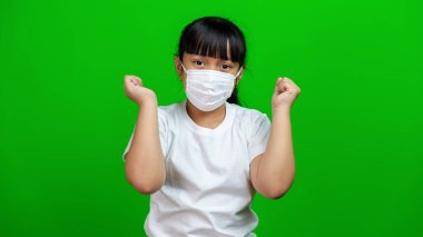 Maske takan Asyalı çocuk kendini mutlu hissediyordu. Fırsat buldukça rahatlamıştı. Çekici gülümseyen Asyalı çocuk yumruk pompası, evet diyerek zafer kazanmak, yeşil arka planda durmak harika bir sonuçla tatmin olmak.