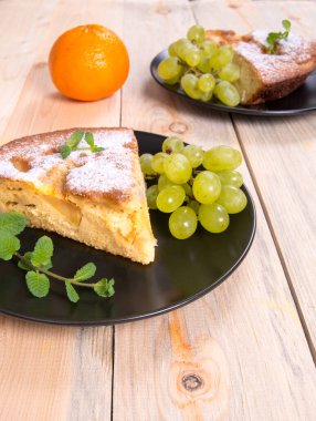 Charlotte, üzerinde nane filizi, portakal, üzüm ve elma olan elmalı turta. Tahta bir masada siyah bir tabakta. Kopya alanı, yakın plan, fotoğraflar, duvar kağıdı.