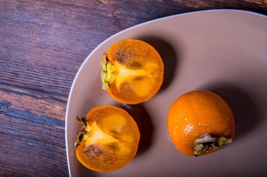 Hurma ağacı, ahşap bir masanın üzerindeki bir tabakta ikiye bölünmüş, yakın plan, kopyalama alanı