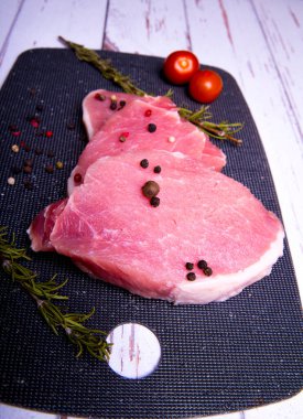 Domuz eti. Siyah pirzola tahtasında taze domuz bifteği ve baharatlı, kiraz domatesli, biberiyeli, biberli, biberli, kopyalama alanlı.