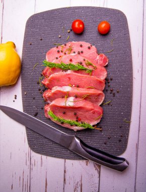 Domuz eti. Siyah kesim tahtasında taze domuz bifteği ve baharatlar, kiraz domatesleri, biberiye, biber, ayva, bıçak, kopyalama alanı