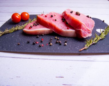 Domuz eti. Siyah pirzola tahtasında taze domuz bifteği ve baharatlı, kiraz domatesli, biberiyeli, biberli, biberli, kopyalama alanlı.