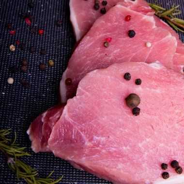 Domuz eti. Siyah kesim tahtasında taze domuz bifteği ve baharatlar, biberiye, biber, biber, kopyalama alanı.