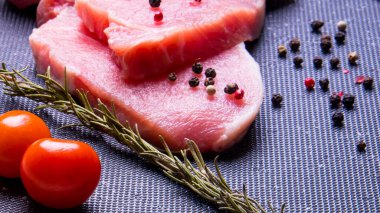 Domuz eti. Siyah pirzola tahtasında taze domuz bifteği ve baharatlı, kiraz domatesli, biberiyeli, biberli, biberli, kopyalama alanlı.