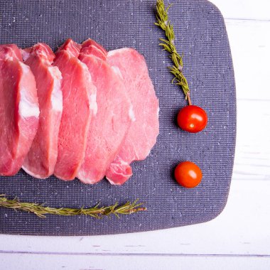 Domuz eti. Siyah pirzola tahtasında taze domuz bifteği ve baharatlı, kiraz domatesli, biberiyeli, biberli, biberli, kopyalama alanlı.