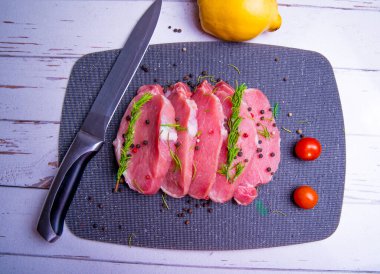 Domuz eti. Siyah kesim tahtasında taze domuz bifteği ve baharatlar, kiraz domatesleri, biberiye, biber, ayva, bıçak, kopyalama alanı