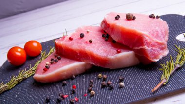 Domuz eti. Siyah pirzola tahtasında taze domuz bifteği ve baharatlı, kiraz domatesli, biberiyeli, biberli, biberli, kopyalama alanlı.