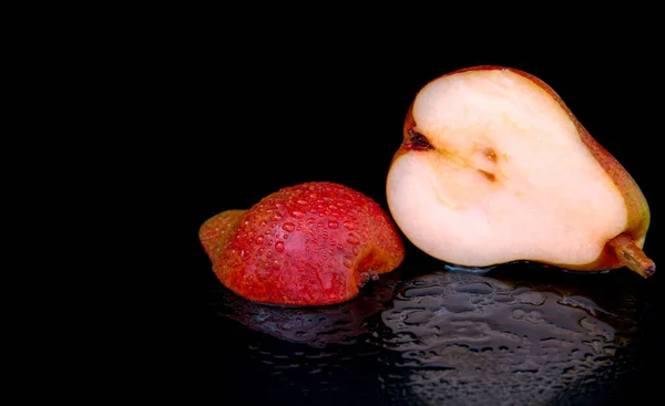 Red pear cut in half with water drops on a black background, close-up, copy space, template