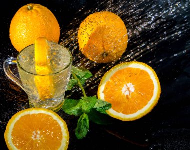 Siyah arka planda portakal suyu ve nane aromalı bir bardağa sıçrıyor, sağlıklı yaşam tarzı konsepti, fotokopi alanı, havada durma.