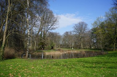 Berlin, Almanya - 9 Nisan 2023: 19. yüzyıl Biesdorf Sarayı veya Schloss Biesdorf Sarayı 'nda yürüyüş yolları olan Schlosspark Biesdorf ormanlarında yer alan gölet manzarası.