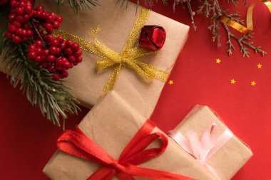 Güzel bir Noel kompozisyonu, hediye paketi, kurdele, hediyeler ve kırmızı arka planda köknar dalları. Düz yatıyordu