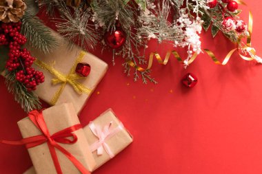 Güzel bir Noel kompozisyonu, hediye paketi, kurdele, hediyeler ve kırmızı arka planda köknar dalları. Kopyalama alanı olan düz.