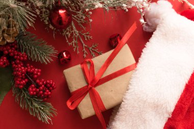 Güzel bir Noel kompozisyonu, hediye paketi, kurdele, hediyeler, Noel Baba şapkası ve kırmızı arka planda köknar dalları. Düz yatıyordu