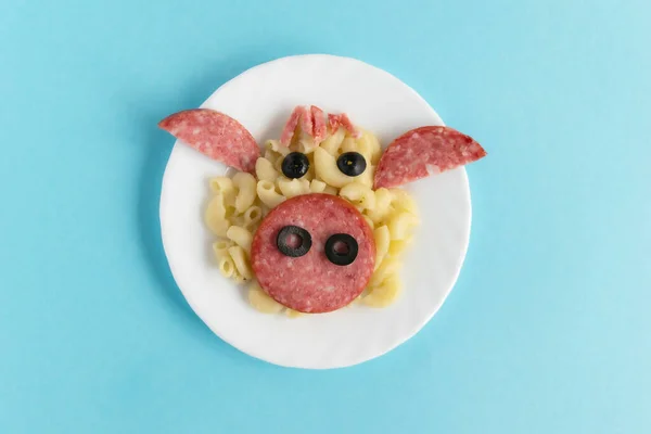 Funny Breakfast, lunch or dinner for children in the form of a bull\'s face made of pasta, sausage, bacon, olives and fresh tomatoes on a blue background. Instruction how to make creative food art breakfast for kids. Step 6. Top view.