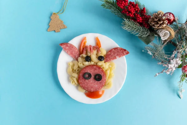 Funny Breakfast for children in the form of bulls face made of pasta, sausage, bacon, olives and fresh tomatoes on a blue background. Plate with creative food art Breakfast for children
