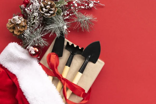 Noel ve yeni yıl kompozisyonu bahçe aletleri, kürek ve tırmık ve kırmızı arka planda Noel Baba şapkası. Bahçe işleri ve kart, takvim ve kapsama alanları için çiftçilik. Üst manzara, düz uzanma