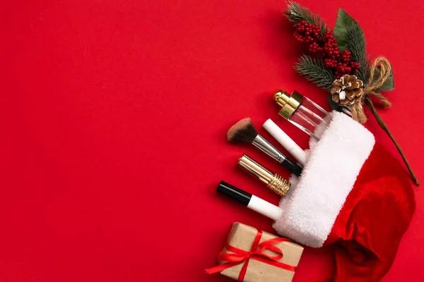 Makyaj ürünleri ve kırmızı kağıtta Noel dekoru olan düz bir kompozisyon. Xmas, mutlu yıllar 2021, kadın dilekleri konsepti. Üst görünüm, alanı kopyala