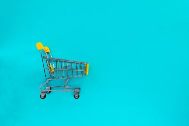 Boş market arabası ve mavi arka planda cep telefonu. İş anlayışı, alışveriş, online alışveriş, kara Cuma satışları. Üst görünüm düz konum
