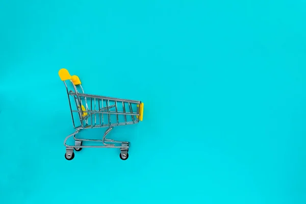 Boş market arabası ve mavi arka planda cep telefonu. İş anlayışı, alışveriş, online alışveriş, kara Cuma satışları. Üst görünüm düz konum