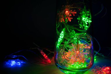 Koyu arkaplanda camda renkli, birbirine dolanmış yılbaşı kar taneleri ışıkları. Mutlu Noeller ve mutlu yıllar konsepti