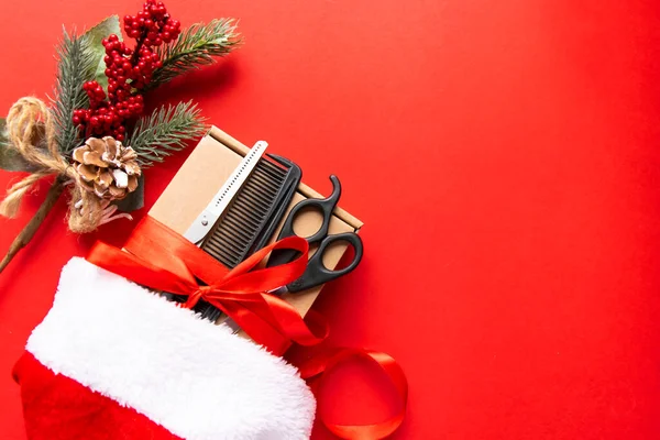 Noel kompozisyonu düzdü. Kuaför aletleri, hediye ve Noel Baba şapkası takan kırmızı arka plan. Xmas, mutlu yıllar. Boşluğu kopyala.