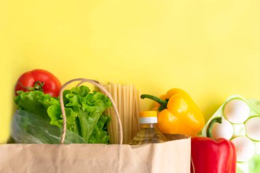 Coronavirus sırasında sağlıklı yemek teslimatı. Kese kağıdında sarı arka plan için gıda bağışı. Muhtelif konserve yiyecekler, tahıllar, makarna ve sebzeler ile karton kutuya yardım et. Gönüllü kutusu. Boşluğu kopyala