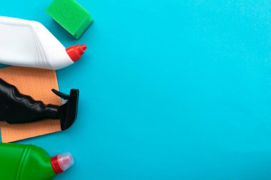 Mavi arka planda ev temizleme malzemeleri. Temizleme sıvısı ve süngerli sıra sıra plastik şişeler, üstüne de kopyalama alanı. Temizlik işi, üretim, alışveriş ve teslimat.
