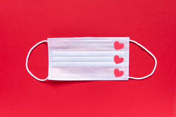 Creatieve platte lay Valentijnsdag compositie. Medisch gezichtsmasker versierd met rode harten op rode achtergrond. Kopieer ruimte.. — Stockfoto