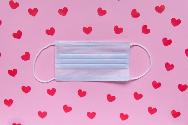 Creatieve platte lay Valentijnsdag compositie. Medisch gezichtsmasker versierd met rode harten op roze achtergrond. Kopieer ruimte.. — Stockfoto