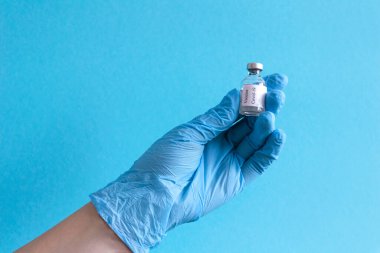 Koruyucu mavi eldivenler verin mavi arka planda ilaç aşısı şişesi bulundurun. Aşı ve sağlık hizmetleri kavramı. Metin için boşluk