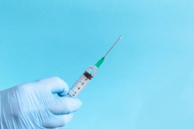 Koruyucu mavi eldivenleri teslim et mavi arka planda aşılı ilaç şırıngası tut. Aşı ve sağlık hizmetleri kavramı. Metin için boşluk