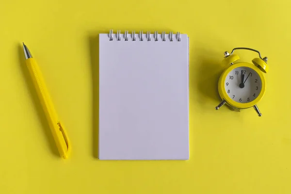 Clean Notepad, clock and pen on a yellow background, spiral notebook on the table. Business, training, education. Monochrome yellow and minimalism. Flatlay, top view.