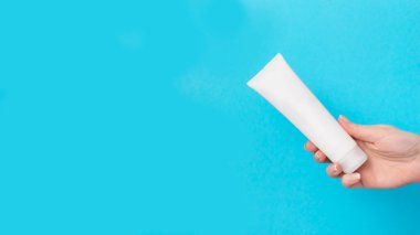 Kadınların elinde mavi arka planda beyaz krema tüpü var. Güzellik konsepti, temiz ve bakımlı kozmetik.