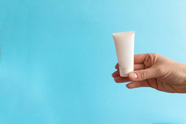 Kadınların elinde mavi arka planda beyaz krema tüpü var. Güzellik konsepti, temiz ve bakımlı kozmetik.