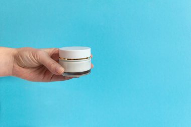 Kadınların elinde mavi arka planda beyaz krema tüpü var. Güzellik konsepti, temiz ve bakımlı kozmetik.