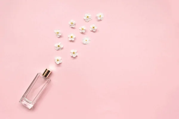 Butelka kobiecych perfum z białymi wiśniowymi kwiatami na różowym tle. — Zdjęcie stockowe