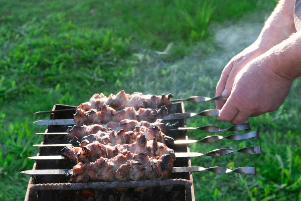 Mãos masculinas segurando um espeto com churrasco na grelha — Fotografia de Stock