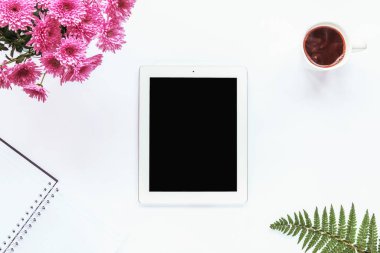 Tablet bilgisayar, defter, bir fincan kahve, bir buket pembe kasımpatı ve beyaz arka planda eğreltiotu yaprakları. Samimi iş yeri, üst görünüm, kopyalama alanı.