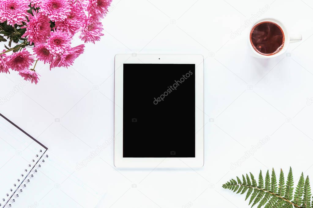 Tablet computer, notebook, cup of coffee, bouquet of pink chrysanthemums and fern leaves on a white background. Cozy workplace, top view, copy space.