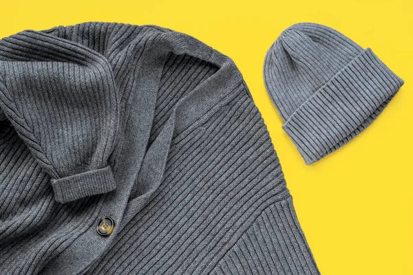 Gray cardigan sweater and cap on yellow background. Trendy colors of the year 2021. Top view, flat lay