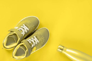 Sarı arka planda su olan gri spor ayakkabılar ve şişe. Sağlıklı yaşam, spor ve eğitim kavramı, üst görüş, kopyalama alanı. Modaya uygun renklerde