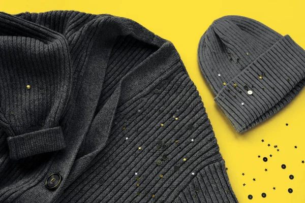 Gray cardigan sweater and cap on yellow background with confetti. Trendy colors of the year 2021. Top view, flat lay.