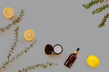 Markasız cam şişeler, sarı limon meyveleri ve gri arka planda okaliptüs dalları. Ev spa konsepti. Üst görünüm, düz görünüm, kopyalama alanı. Renk 2021 Aydınlatıcı ve Nihai Gri